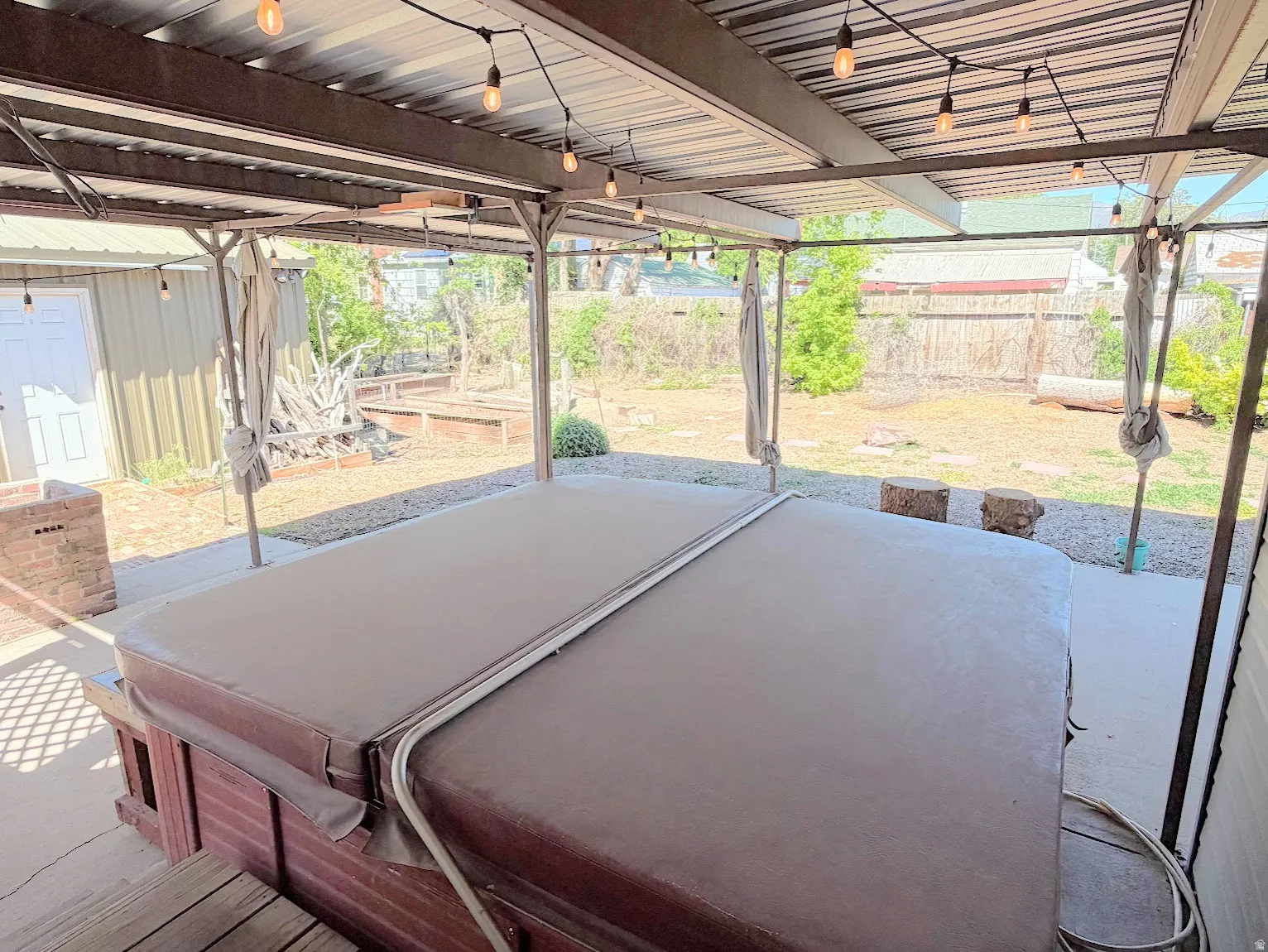 Covered patio area with a hot tub, string lighting, a concrete surface, and a wooden fence