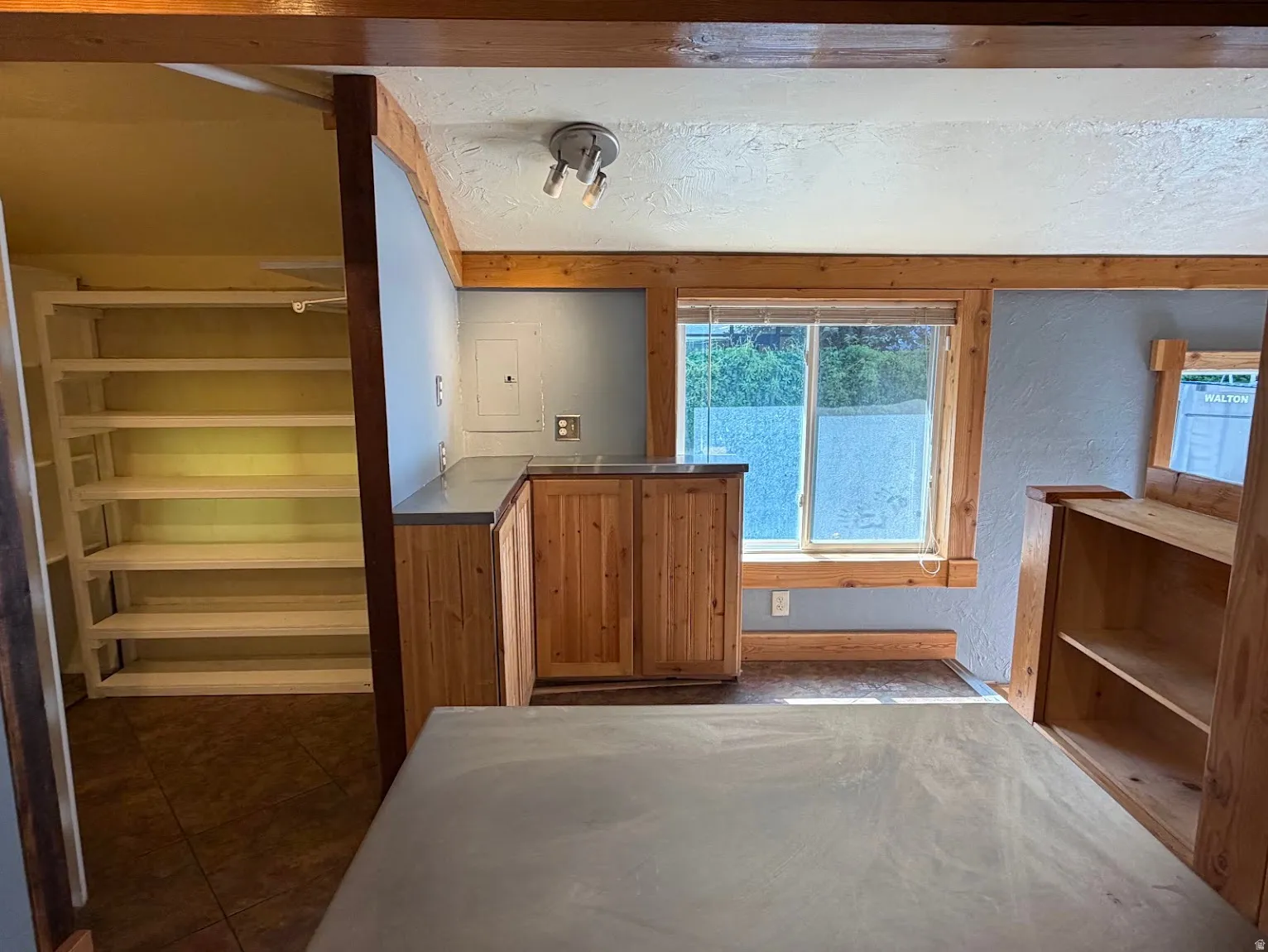 Wood-finish cabinetry with gray countertops, wood-trimmed window, built-in shelving, and track lighting