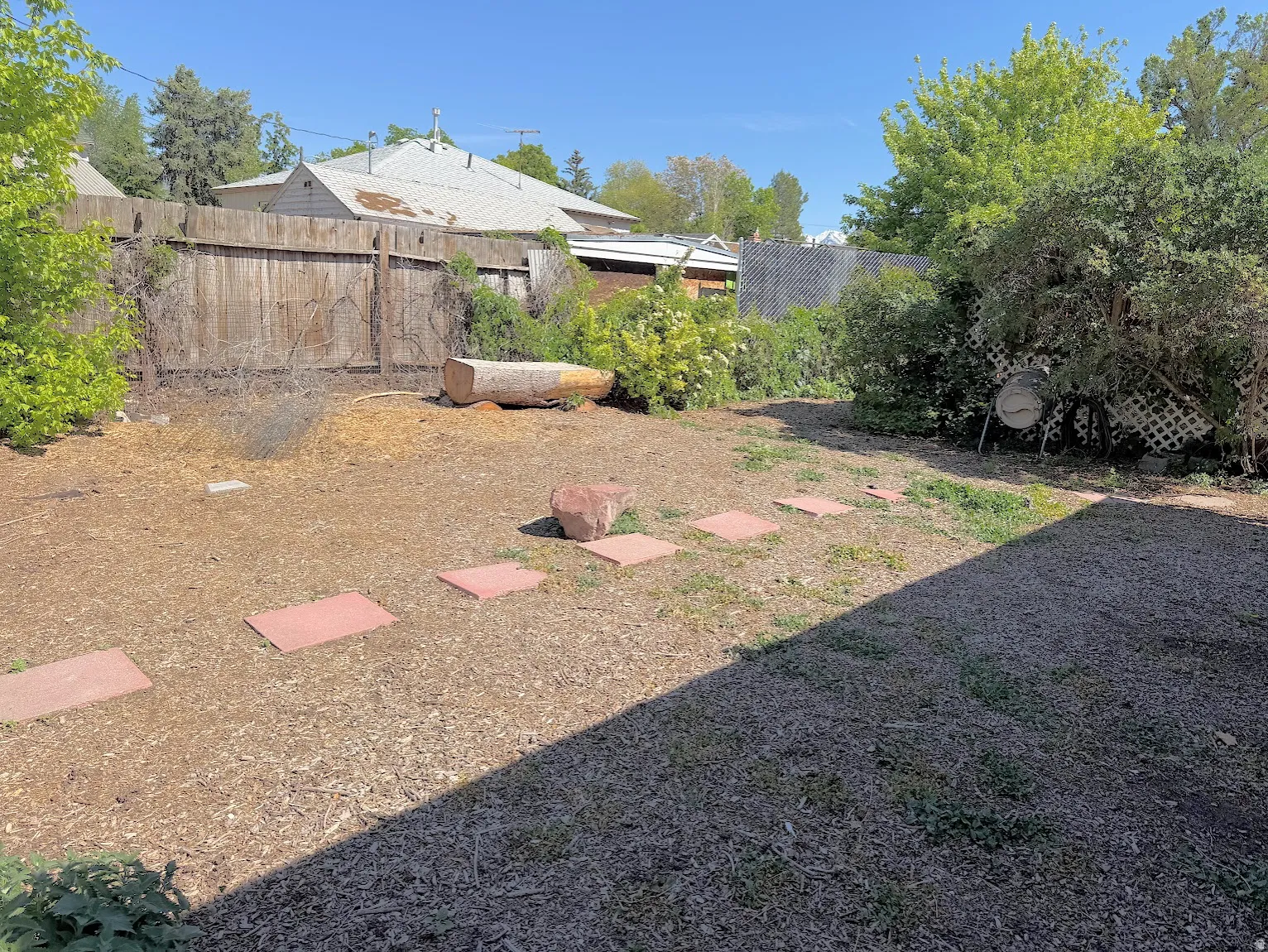 Expansive outdoor space featuring a wood fence, mature perimeter landscaping, and a path of stepping stones