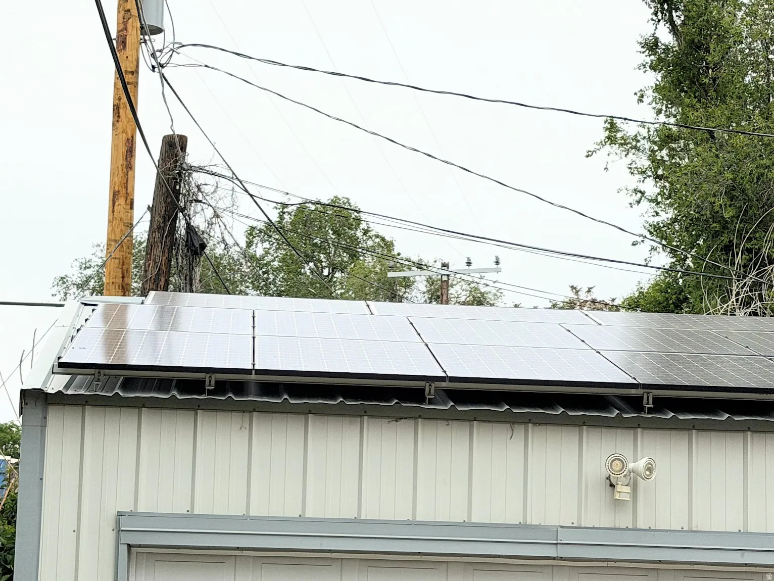 Rooftop solar panel array on a white corrugated metal building with a security light fixture