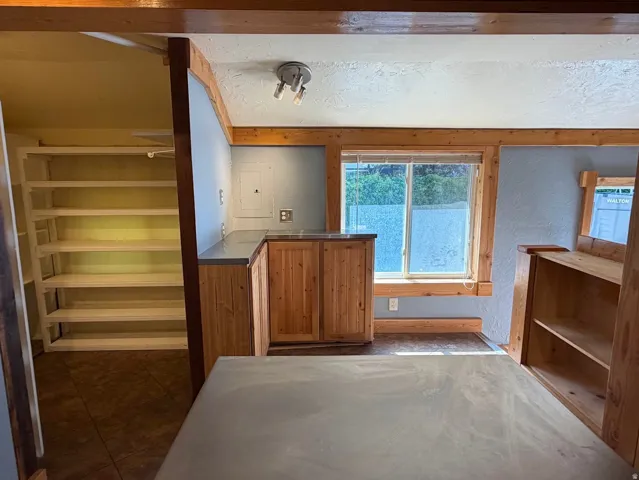 Wood-finish cabinetry with gray countertops, wood-trimmed window, built-in shelving, and track lighting