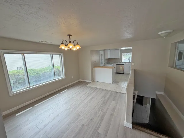 Open-concept living and dining area featuring wood-finish flooring, large multi-pane windows with natural light, and a pendant light fixture