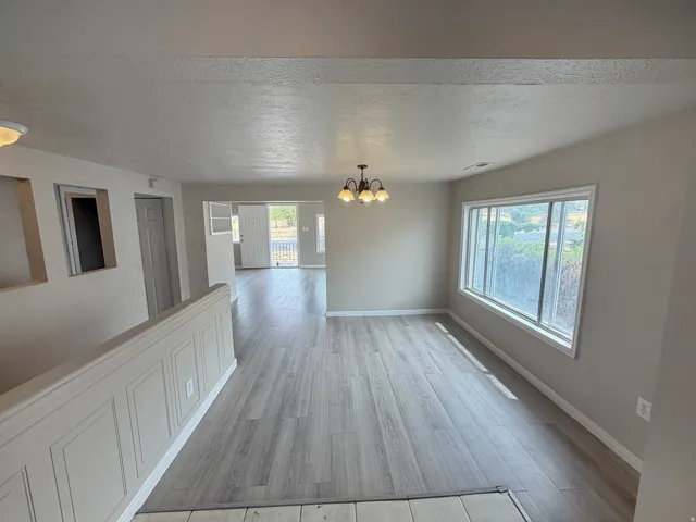Wood-finish flooring throughout, large window, ceiling-mounted light fixture, paneling on half-wall, and light-colored wall paint