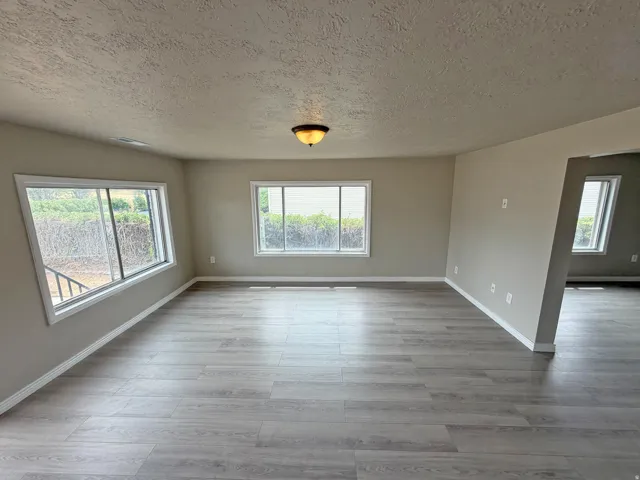 Spacious room with wood-finish flooring, neutral paint, multiple windows, and a semi-flush mount light fixture