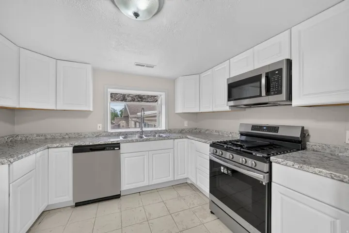 Kitchen featuring white cabinetry, light-toned countertops, tile flooring, a stainless steel gas range, and a stainless steel microwave