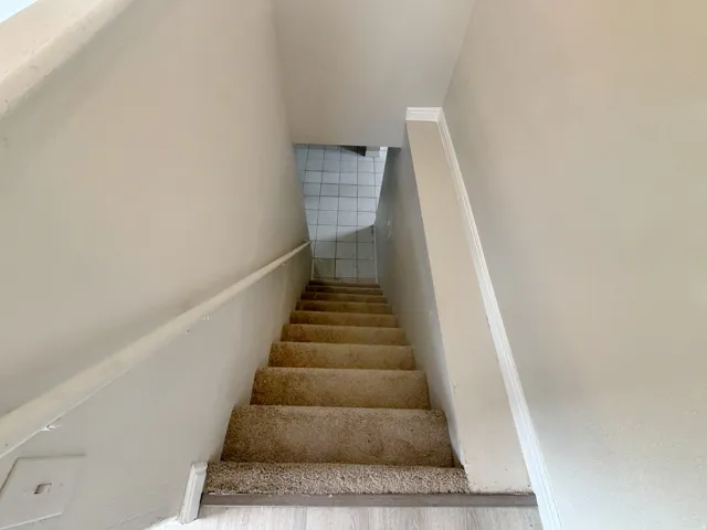 Carpeted staircase with wall-mounted handrail, leading to a tiled lower level