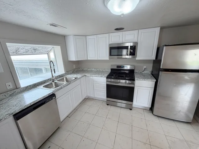 White shaker-style cabinetry, granite-patterned countertops, stainless steel appliances, dual basin sink with gooseneck faucet, and tiled flooring