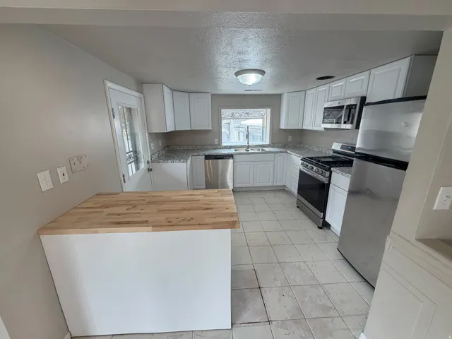 Kitchen featuring stainless steel appliances, white cabinetry, speckled countertops, a built-in island with a wood-finish top, and a tile floor