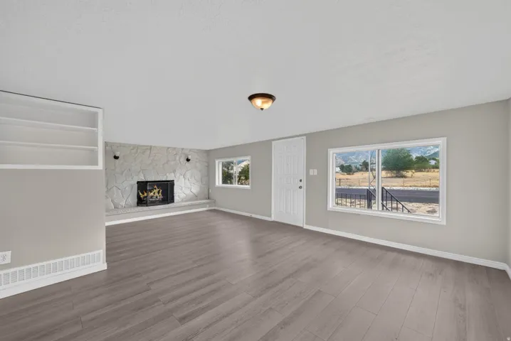 Living space featuring wood-finish flooring, a stone fireplace with hearth, built-in shelving, and multiple windows