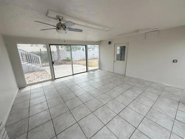 Spacious room with large format tile flooring, ceiling fan with integrated lighting, and sliding glass doors leading to a paved patio