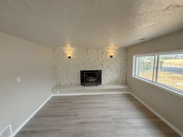 Spacious living area featuring wood-finish flooring, a gas fireplace with marble-look surround and hearth, dual wall sconces with warm lighting, and expansive windows offering natural light and outdoor views