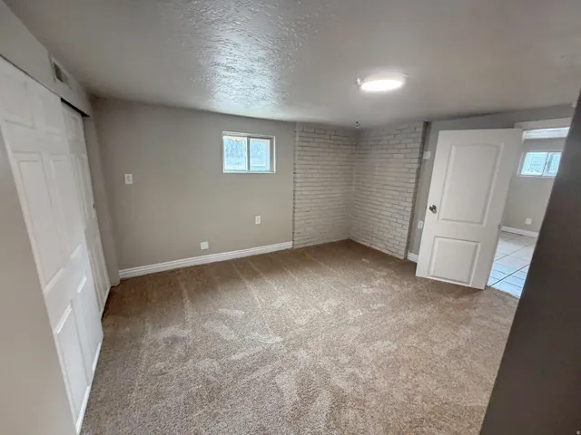 Carpeted flooring, white brick wall accent, single window, white paneled door, and ceiling-mounted light fixture