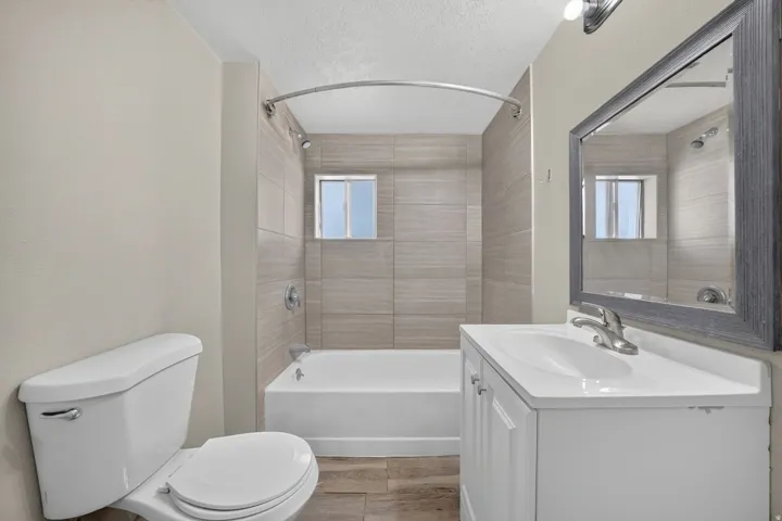 Bathroom featuring a white vanity with a single sink, framed mirror, white toilet, and a bathtub with tiled surround