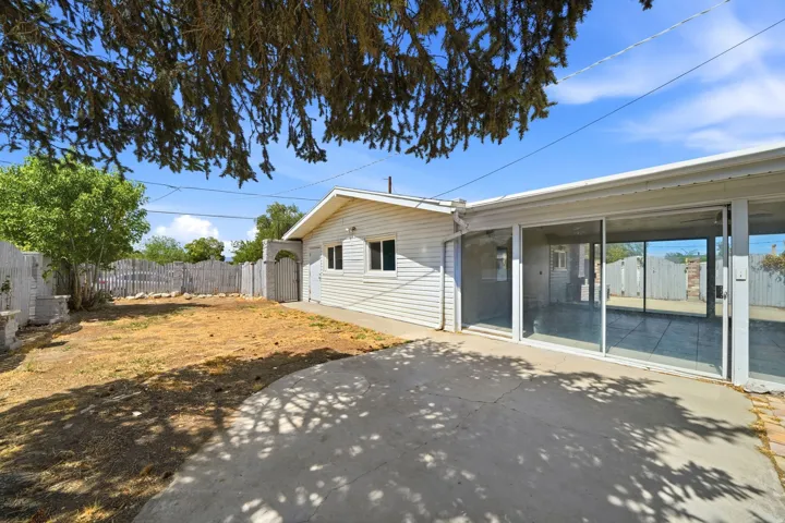 Expansive patio with sliding glass doors, leading to a fenced backyard featuring a wooden arch gate
