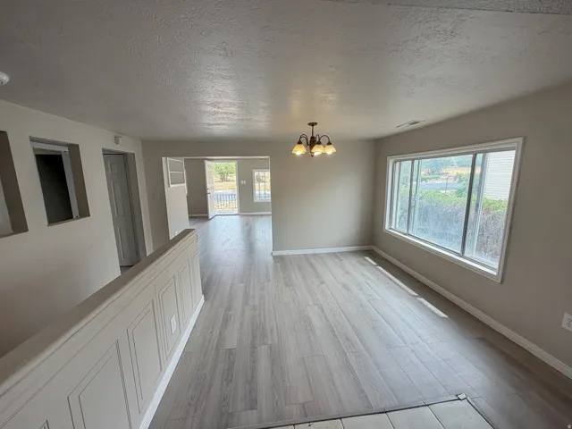 Wood-finish flooring throughout, large window, overhead chandelier, paneled half-wall, and neutral wall paint