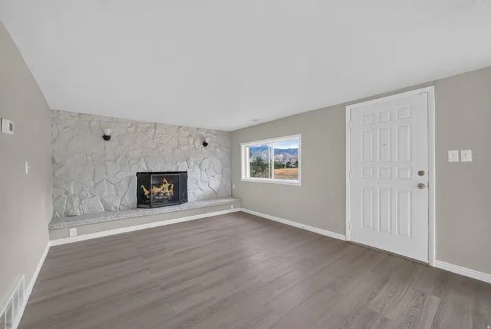 Stone fireplace with integrated hearth, wood-finish flooring, white paneled entry door, and a horizontal window
