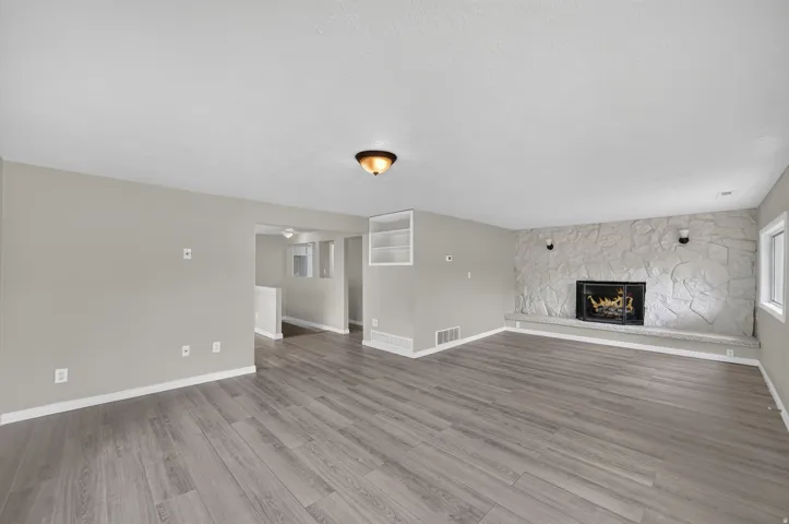 Spacious room featuring wood-finish flooring, a stone-clad fireplace with a hearth, built-in shelving, and a prominent window