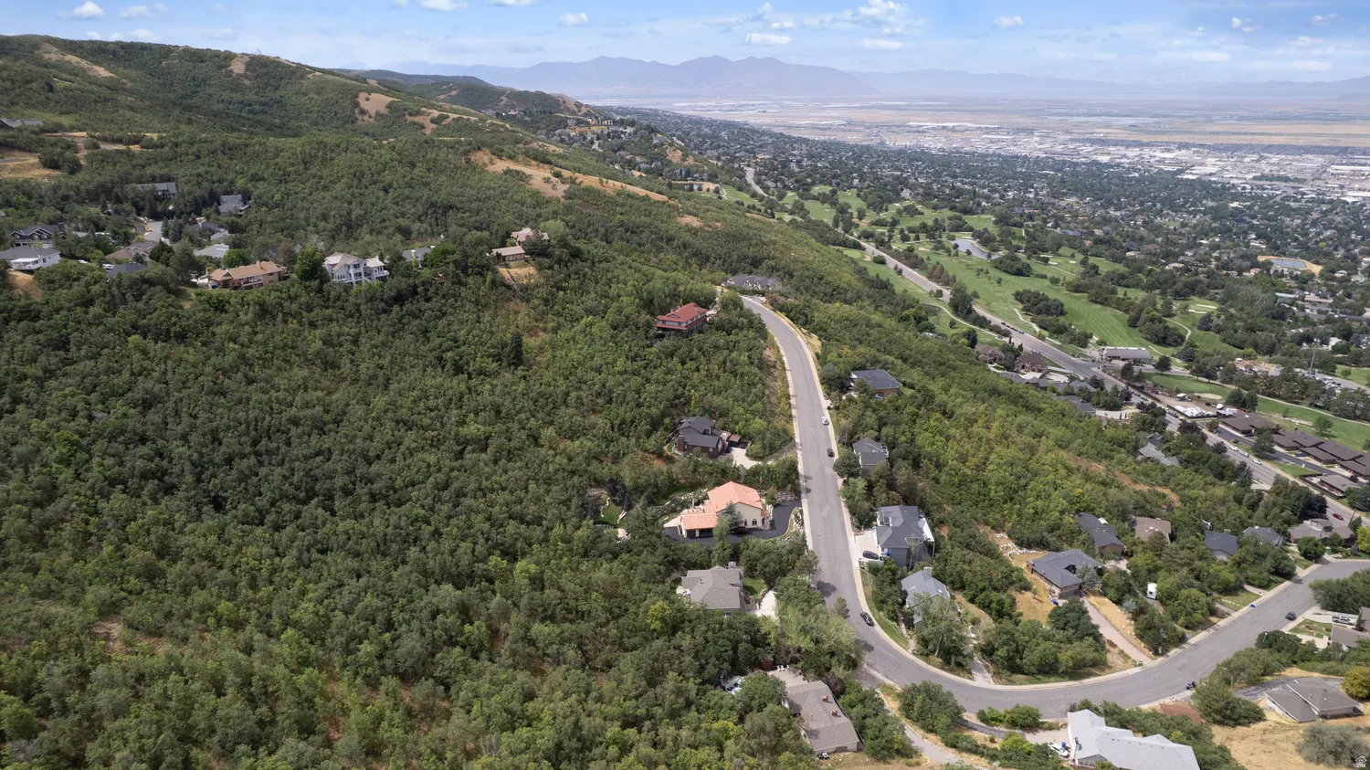 Mountainous terrain with lush green foliage, residential properties, and paved roads