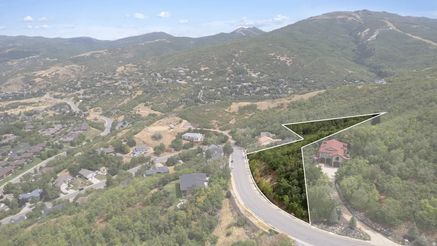 Residential lot bordered by a paved road, surrounded by mature trees, and featuring a mountainous backdrop