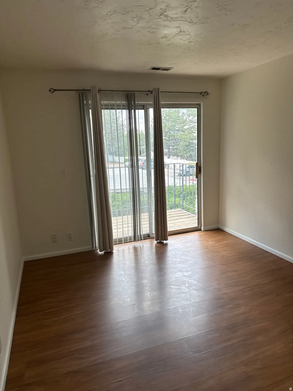 Wood-finish flooring throughout, sliding glass door leading to an outdoor balcony, painted interior walls, and an overhead ventilation register