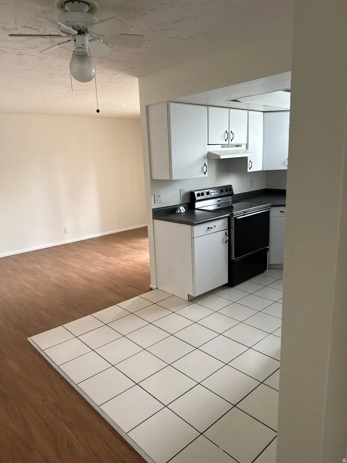 White cabinetry, black countertops, included range, and white tile flooring
