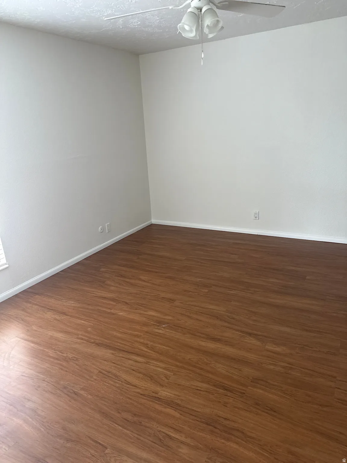 Wood-finish flooring with white trim and a ceiling fan light fixture