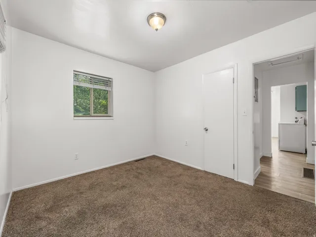 Window with horizontal blinds, overhead flush mount lighting, brown carpet flooring, white painted walls, and a white door with a round knob