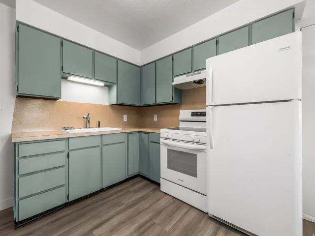 Efficient kitchen featuring sage-green cabinetry with ample storage, wood-finish flooring, and stainless steel appliances including a double wall oven and refrigerator