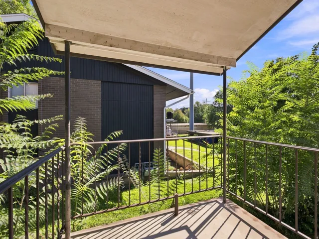 Covered exterior patio with concrete flooring, iron railing, and verdant landscaping