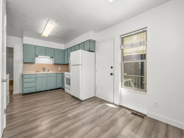 Bright kitchen featuring turquoise cabinetry with ample storage, wood-finish countertops, white refrigerator, and stainless steel appliances