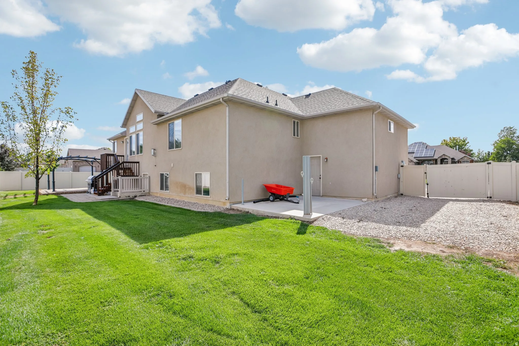 Expansive rear lawn with a stucco exterior, multi-level deck, and full privacy fencing