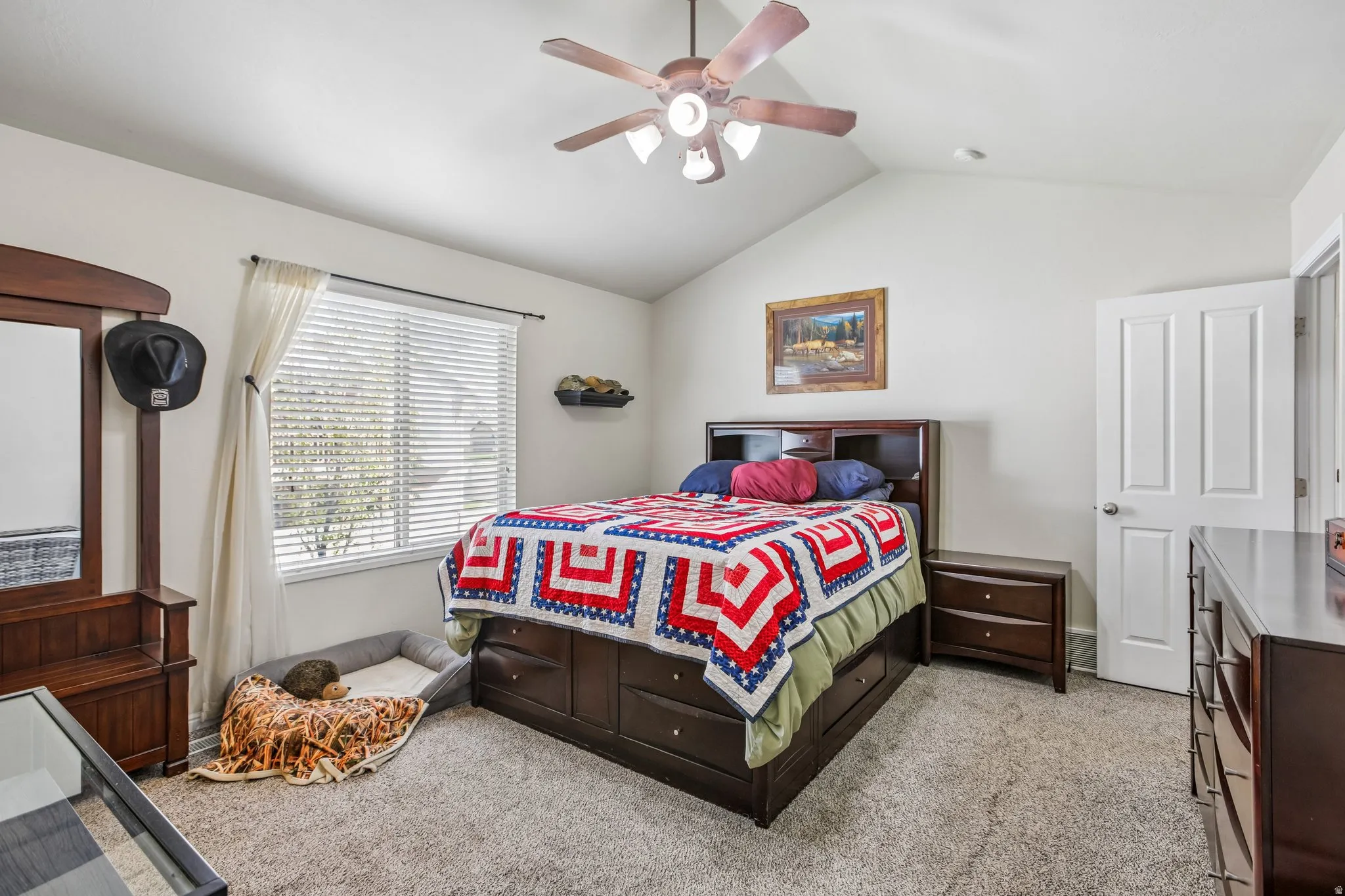 Vaulted ceiling with a ceiling fan, carpeted flooring, large window with blinds, and a white interior door