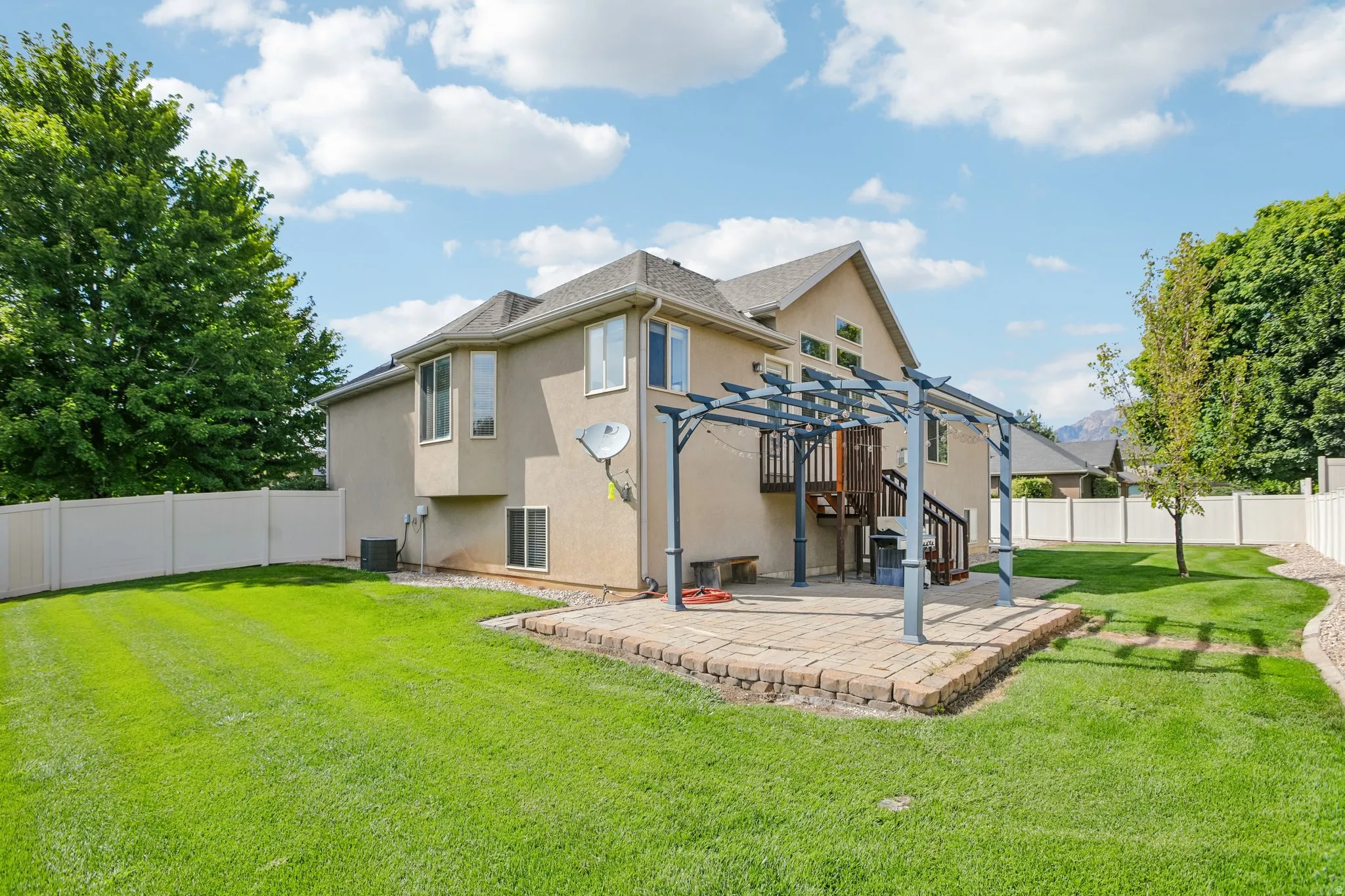 Expansive backyard featuring a manicured lawn, full privacy fencing, and a paver patio with a pergola