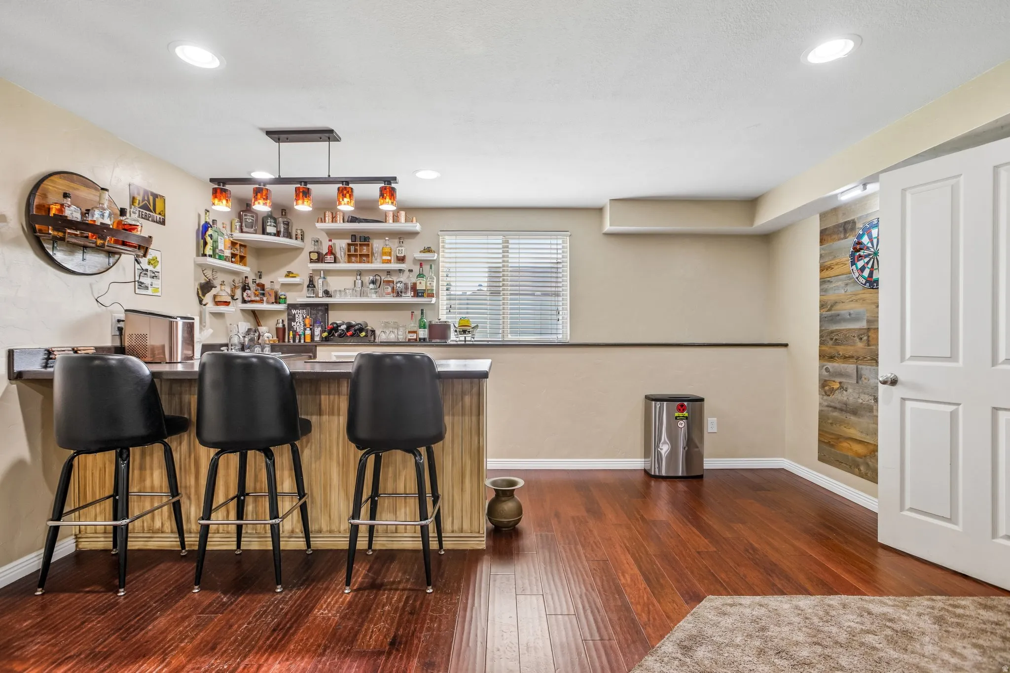 Built-in bar with a dark countertop and wood-finish paneling, overhead pendant lighting, recessed ceiling lighting, and wood-finish flooring