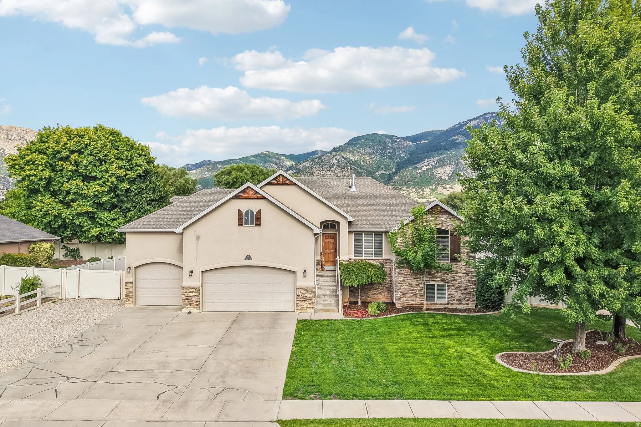 Stucco and stone facade with a multi-car driveway, arched garage doors, and mature landscaping