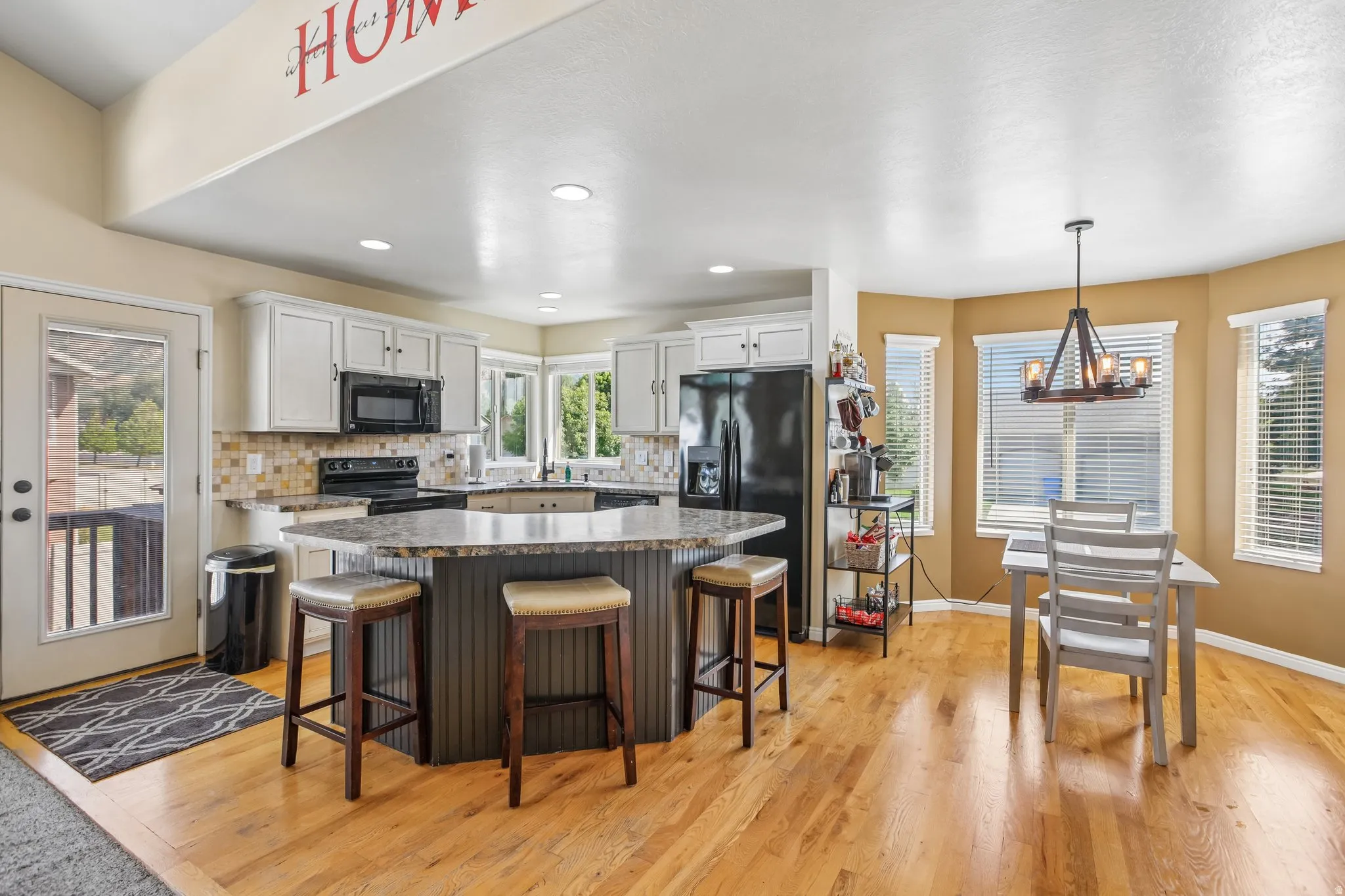 Kitchen with light wood-finish flooring, white cabinetry, a tiled backsplash, and a central island with a stone-finish countertop