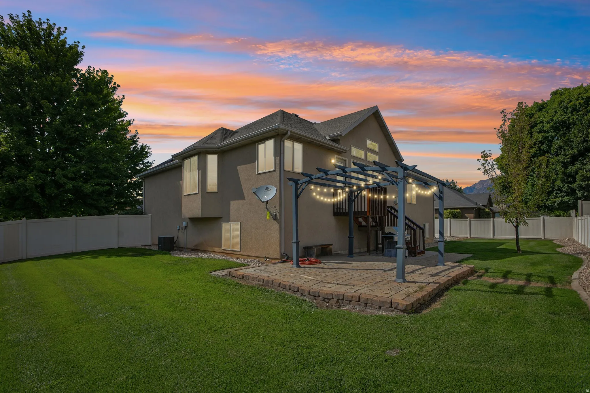 Expansive backyard featuring a manicured lawn, a paver patio with a pergola, and a multi-level deck