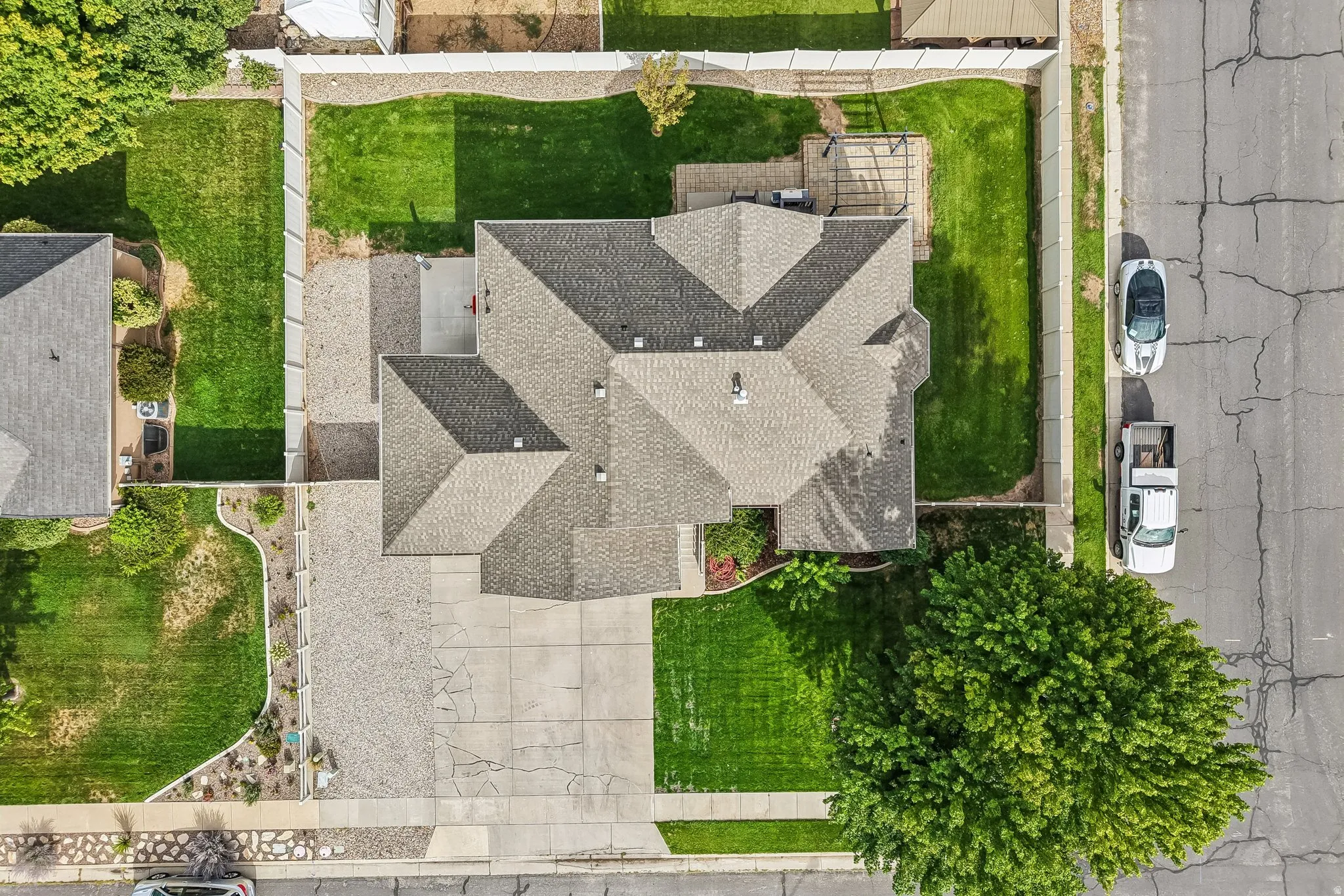 Gabled roofline, concrete driveway, fenced yard, and a paved patio area