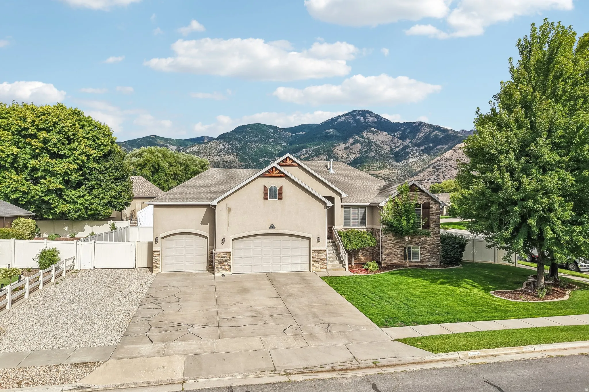 Stucco exterior with stone accents, two-car garage, mature landscaping, and mountain backdrop