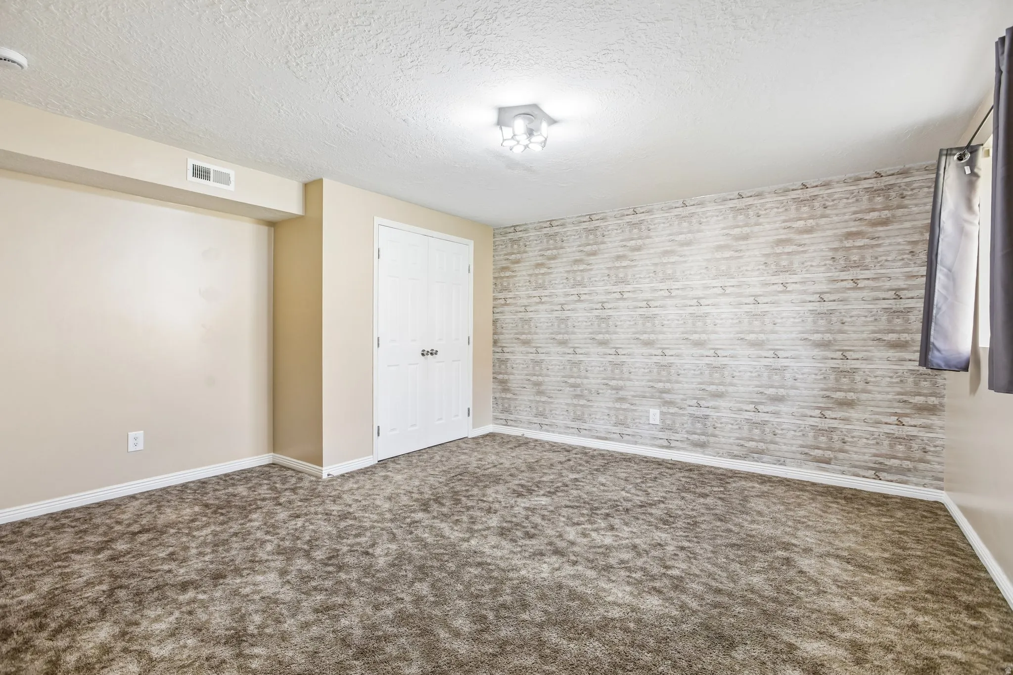 Textured accent wall, neutral carpeting, recessed ceiling light, and built-in closet with bifold doors