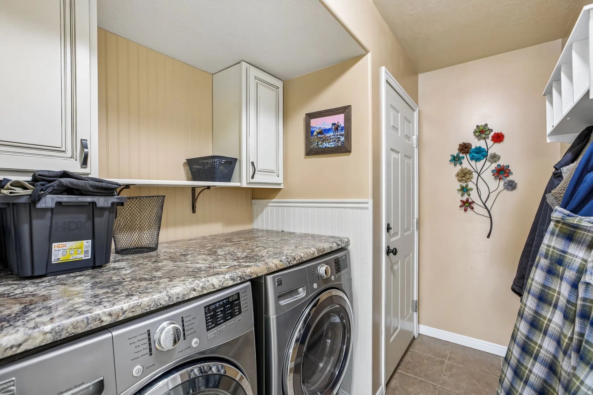 Laundry area featuring a stone-finish countertop, white upper cabinetry, and wainscoting