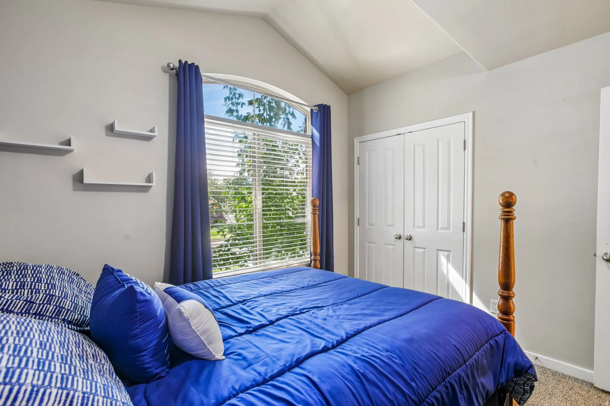 Vaulted ceiling with an arched window, white walls, and built-in wall shelves