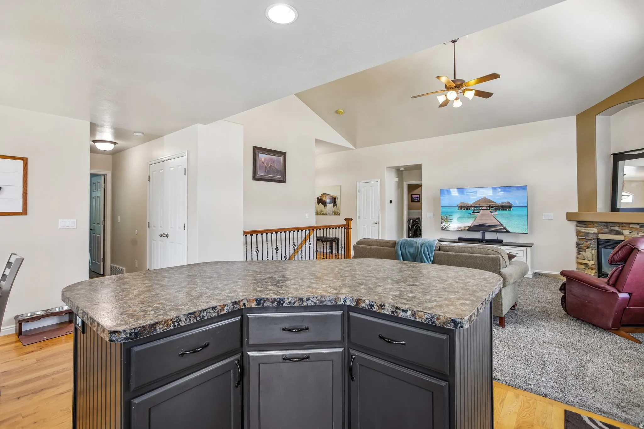 Kitchen island with dark cabinetry and a patterned countertop, wood-finish flooring, vaulted ceiling, and a built-in stone fireplace