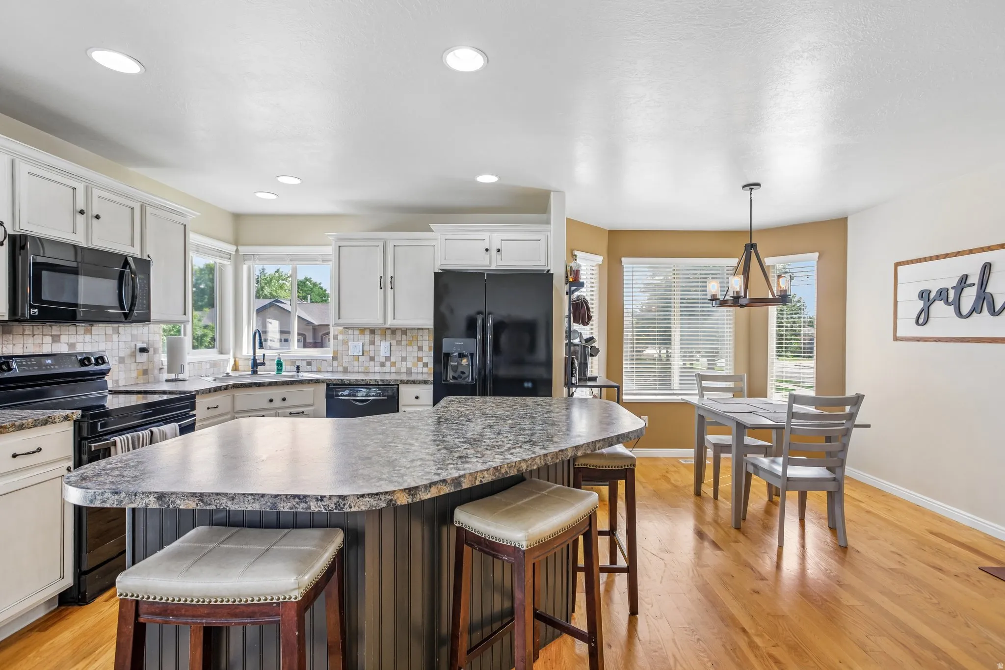 Kitchen featuring white cabinetry, black appliances, a tile backsplash, and a large central island with seating