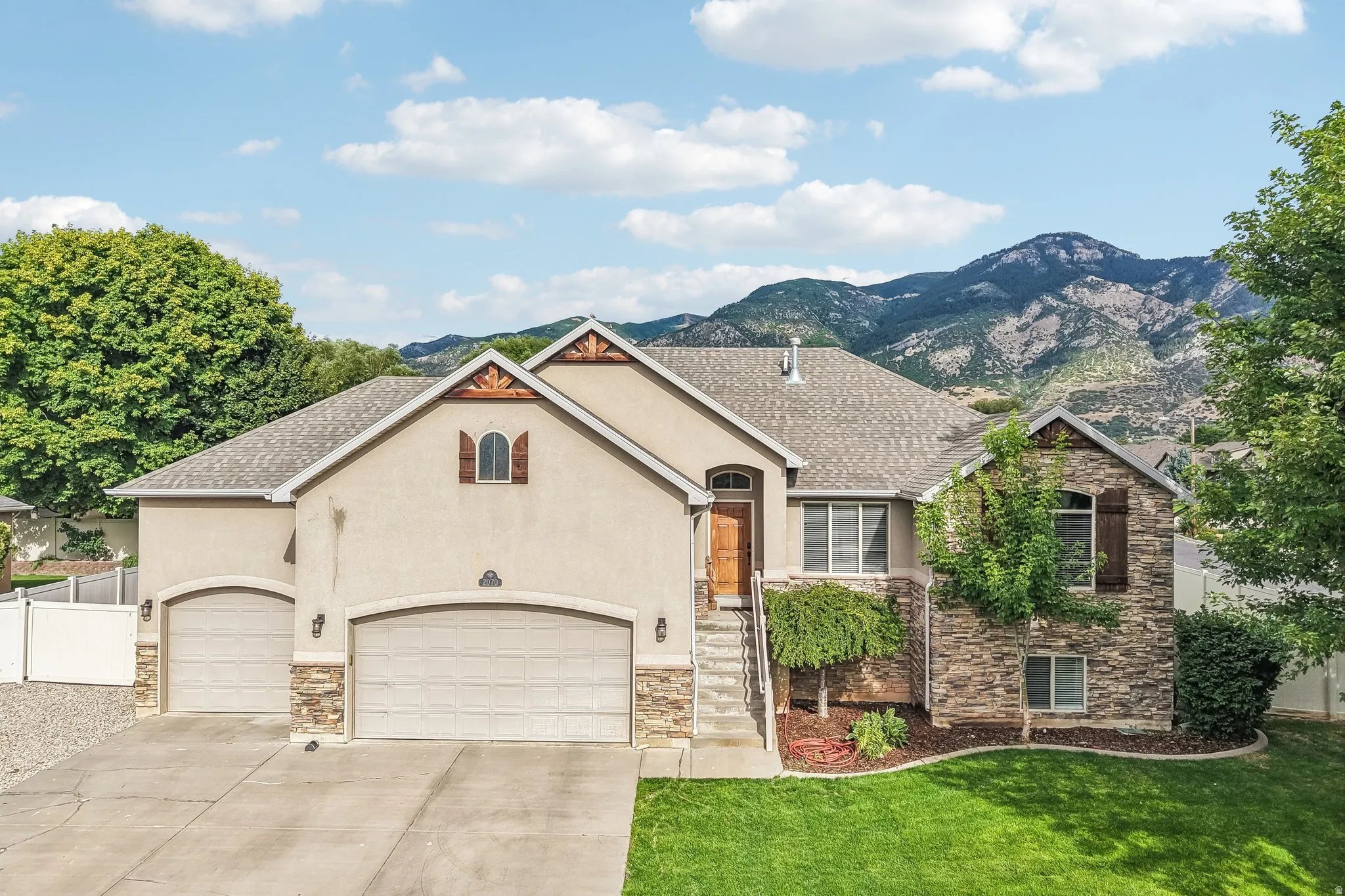 Stucco and stone exterior with architectural gables, mature landscaping, and a three-car garage