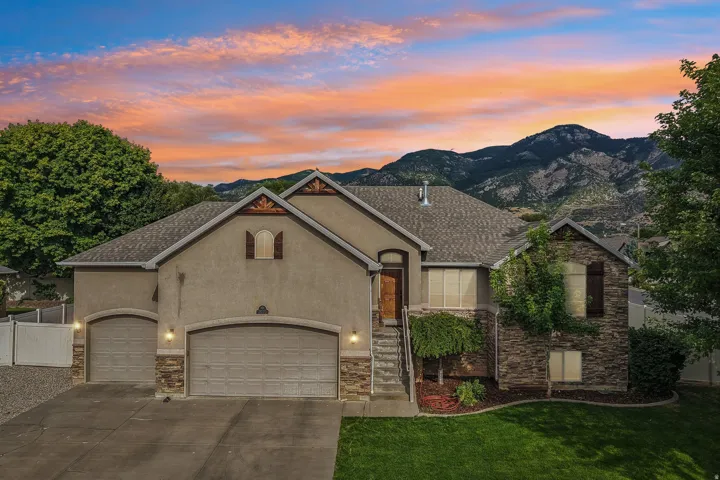 Stucco and stone exterior with a multi-car garage, mature landscaping, mountain backdrop, and prominent front entry