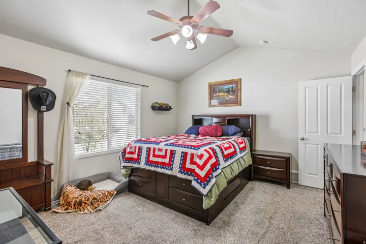 Vaulted ceiling with a ceiling fan, carpeted flooring, large window with blinds, and a white interior door