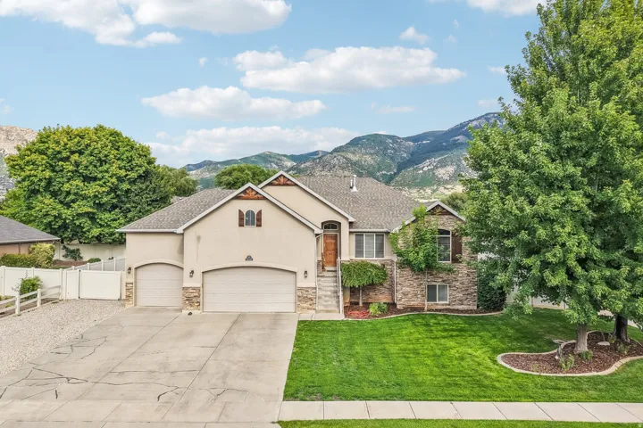 Stucco and stone facade with a multi-car driveway, arched garage doors, and mature landscaping