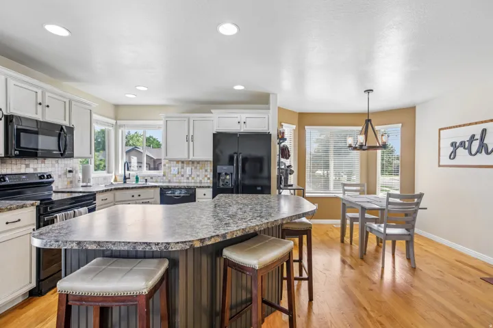 Kitchen featuring white cabinetry, black appliances, a tile backsplash, and a large central island with seating