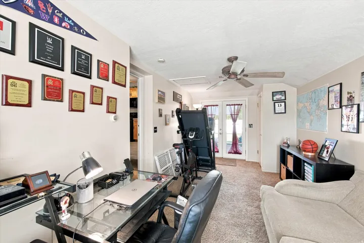 Carpeted room featuring a ceiling fan, a built-in shelving unit, and a set of glass-paned double doors